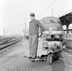 824864 Afbeelding van een stationsassistent van de N.S. in zijn nieuwe uniform met een elektrokar op het N.S.-station ...